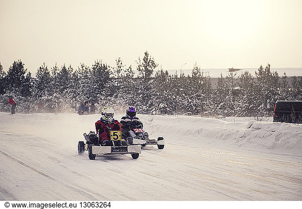 Boys enjoying go-carts racing on snow covered field against sky