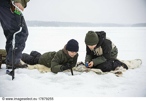 Boys in warm clothing ice fishing at frozen lake during vacation