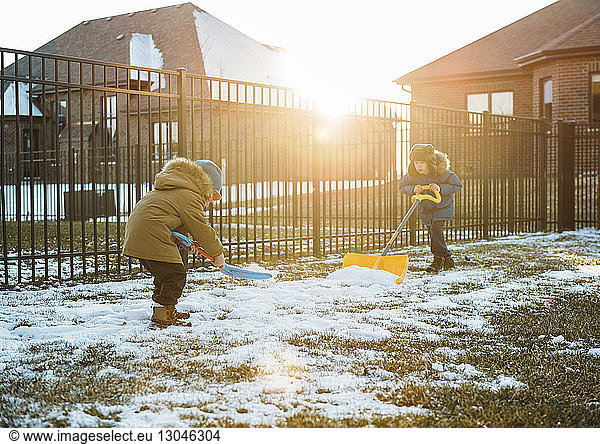 Boys in warm clothing shoveling snow at backyard