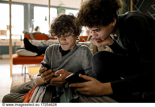 Boys sharing mobile phone while sitting in living room