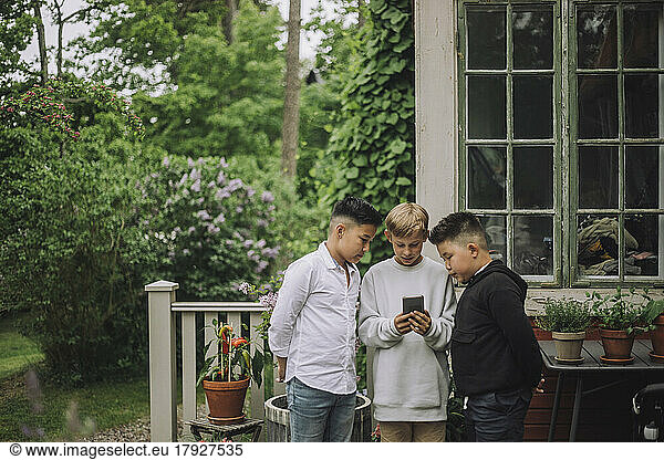 Boys sharing smart phone while standing near house