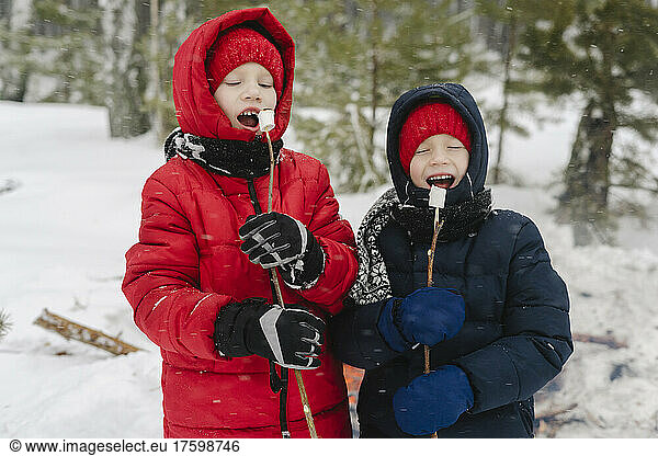 Boys with eyes closed eating marshmallows in snowy forest