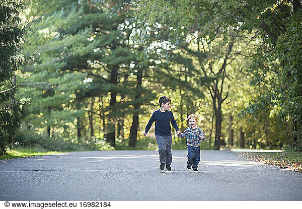 Brüder  die sich glücklich an den Händen halten und eine mit Bäumen gesäumte Straße hinunterlaufen