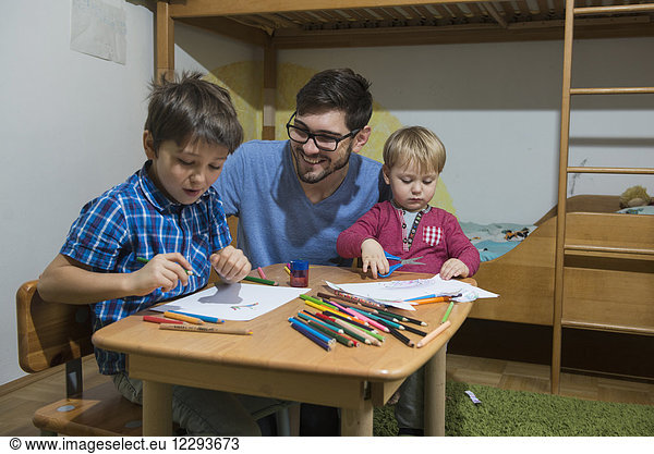 Brüder genießen es  mit Buntstiften zu zeichnen  während der Vater lächelt  München  Deutschland