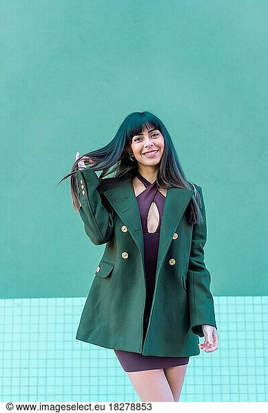 Brünette Modell lächelnd in einem streetyle in einer grünen Jacke. Kaukasierin hübsch ein grüner und blauer Hintergrund