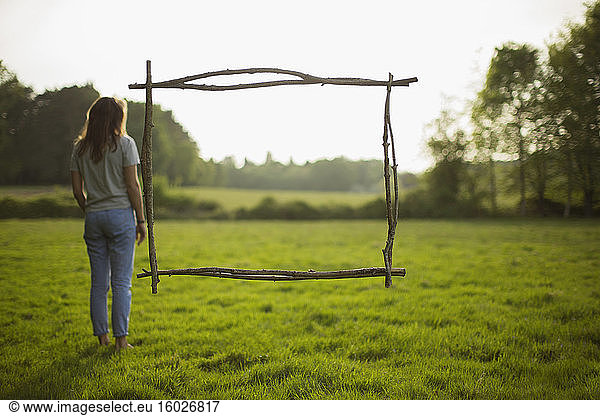 Branch frame over woman standing in idyllic grass field