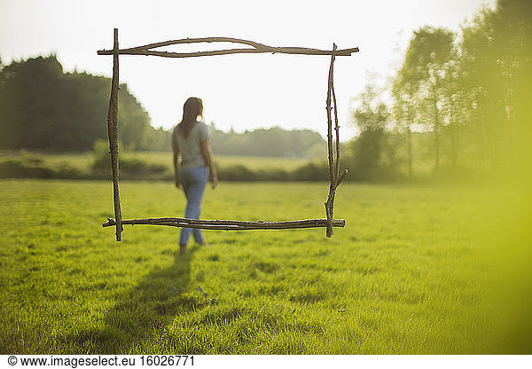 Branch frame over woman walking in idyllic sunny grass field