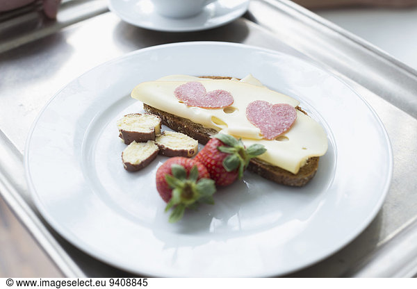 Bread with cheese  strawberry and heart shaped salami on plate  close up