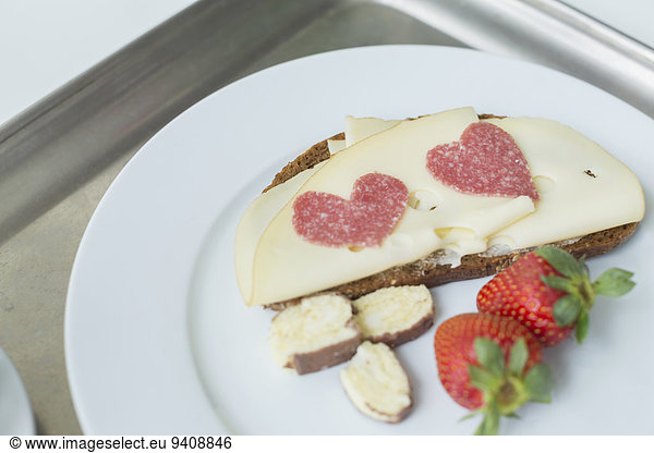 Bread with cheese  strawberry and heart shaped salami on plate  close up