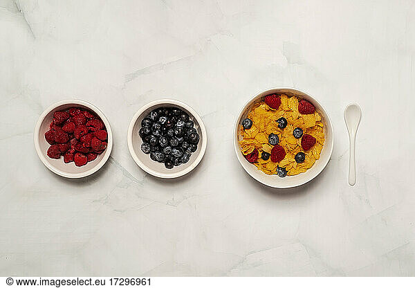 Breakfast cereal with bowls of blueberries and raspberries on marble