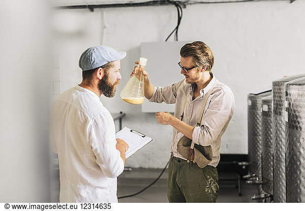 Brewery workers examining beer in beaker
