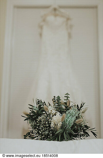 Bridal bouquet on bed with wedding dress in background