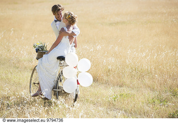 Bride and bridegroom riding bike with balloons attached