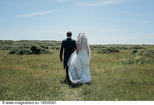 bride and groom walking through a field of green on their wedding day