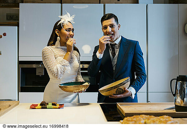 Bride and young groom eating potato chips in kitchen at home