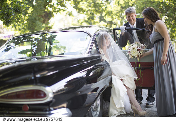 Bride getting out of car before her wedding with driver and maid of honour