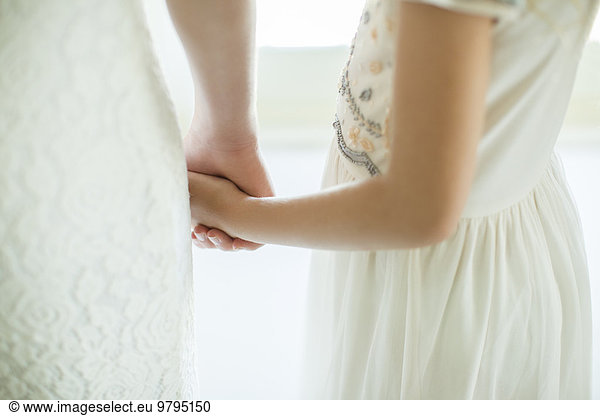 Bride holding bridesmaid's hand in domestic room