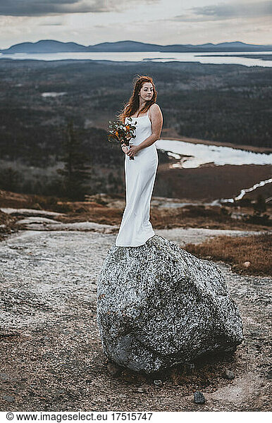 Bride holds wedding bouquet and stands on boulder on mountain