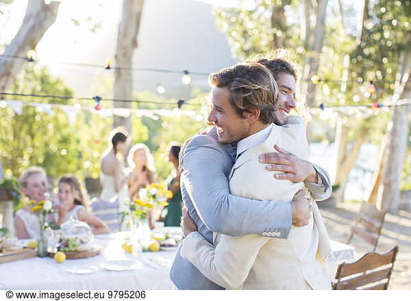 Bridegroom and best man embracing during wedding reception in domestic garden