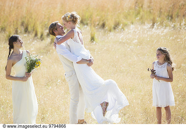 Bridesmaid and bridesmaid watching and laughing Young couple embracing in meadow