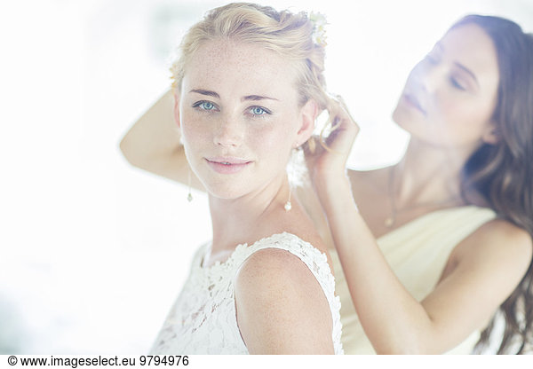 Bridesmaid helping bride with hairstyle in domestic room