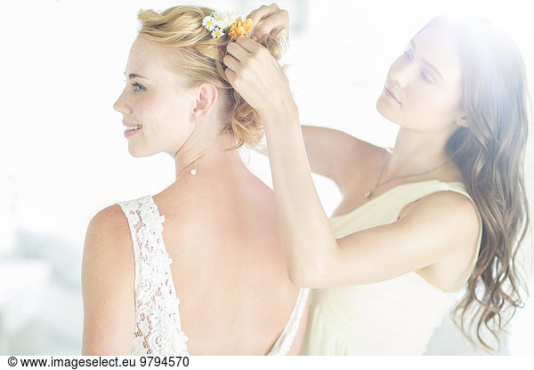 Bridesmaid helping bride with hairstyle in garden