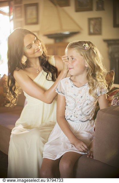 Bridesmaid helping girl with hairstyle in domestic room