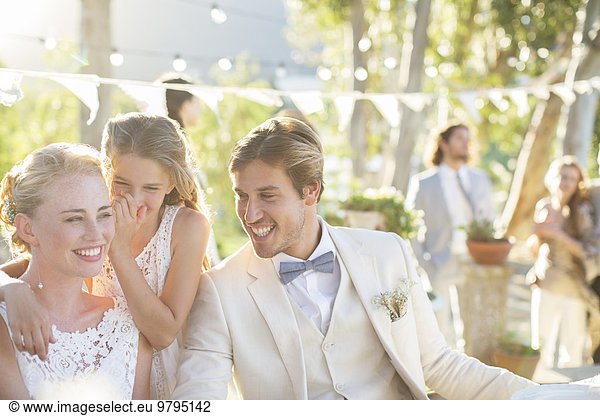 Bridesmaid whispering to bride's ear during wedding reception in domestic garden