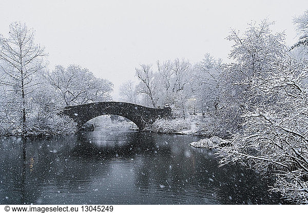 Bridge over lake by bare trees during snowfall
