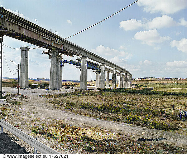 Bridge under construction  pillars and elevated road across an arid landscape.