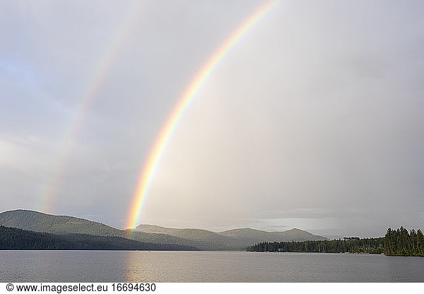 Bright double rainbow over calm lake and forest covered hillside