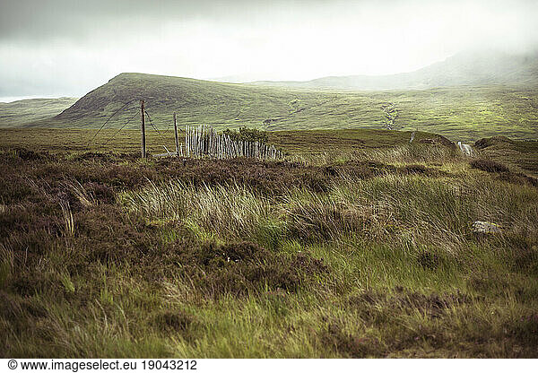 Broken rustic old fence runs through remote misty mountains