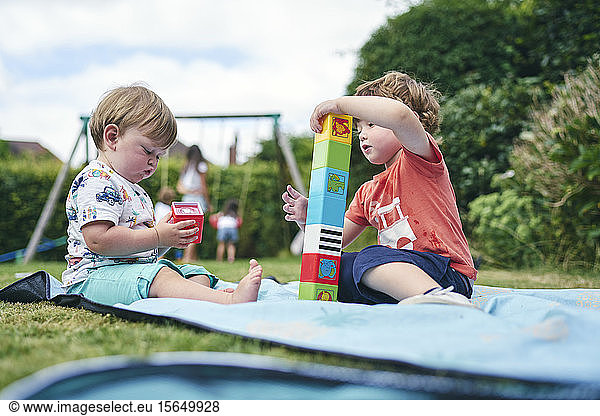Brother and baby sister playing with blocks on picnic blanket