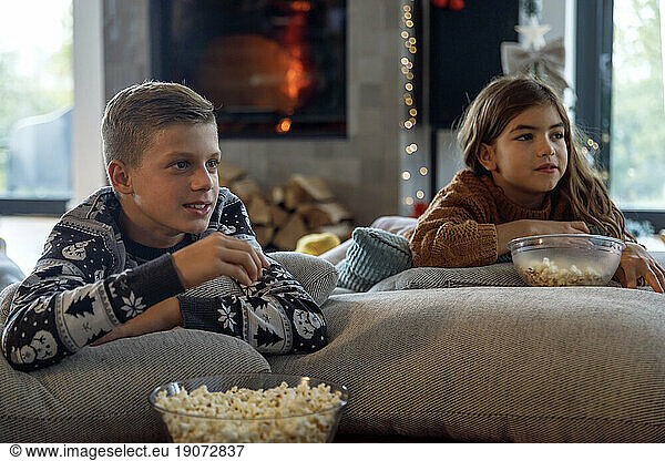 Brother and sister having popcorn and watch TV in living room