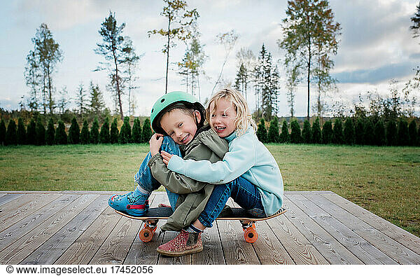 brother and sister hugging on a skateboard playing in the garden