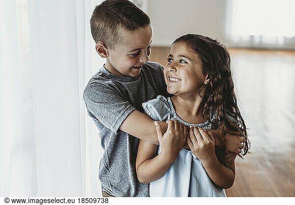 Brother and sister laughing at each other in natural-light studio
