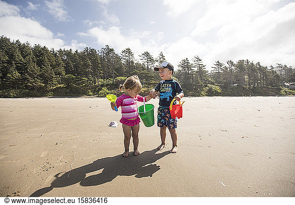 Brother and sister playing at the beach on a windy day.