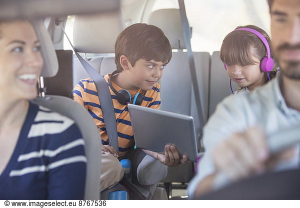 Brother and sister sharing digital tablet in back seat of car