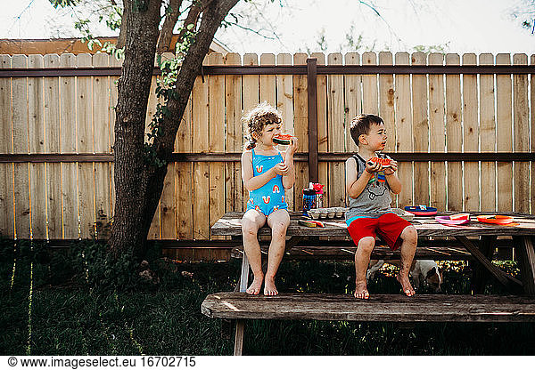 Brother and sister sitting on picnic table eating fresh watermelon