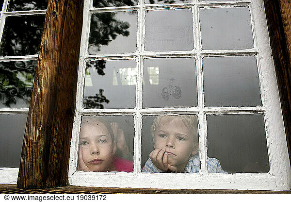 Brother and sister stare forlornly out a cabin window on a gloomy day