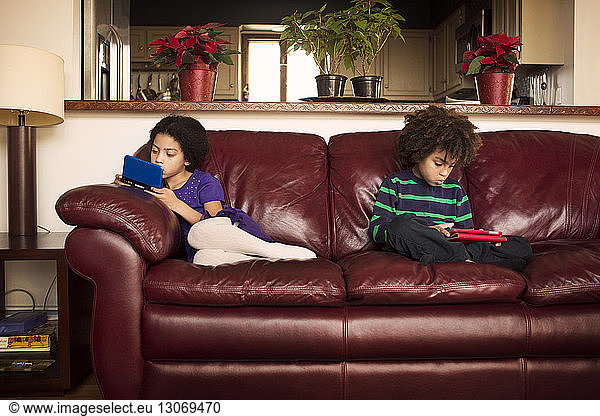Brother and sister using technologies while sitting on leather sofa at home