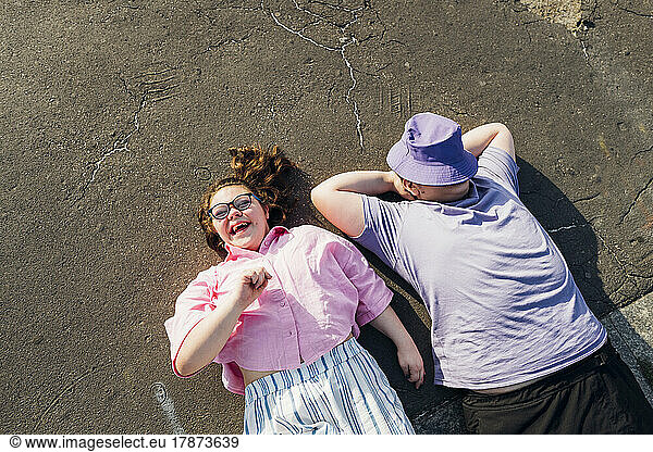 Brother and sister with down syndrome lying on footpath on sunny day