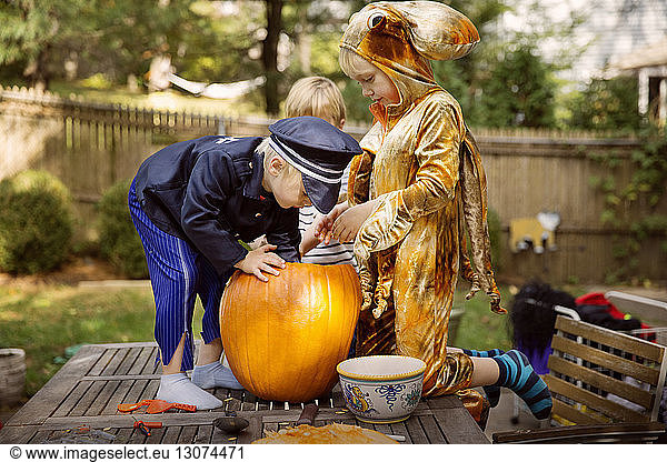 Brothers carving pumpkin on table at yard during Halloween