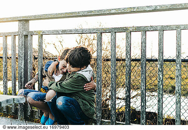 Brothers hug on a wooden park fence during sunrise