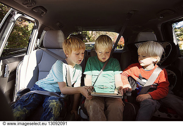 Brothers looking at tablet computer while sitting in car