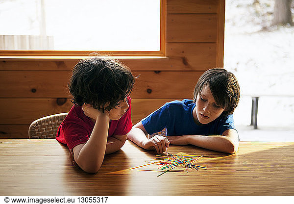 Brothers playing pick up sticks at table in home