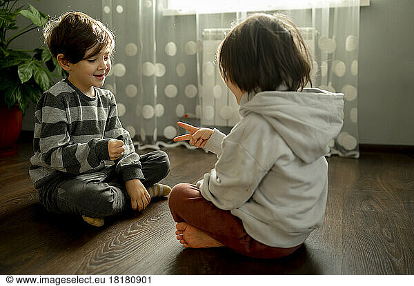 Brothers playing rock paper scissors on floor at home