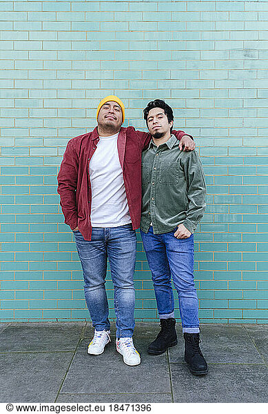 Brothers standing together in front of turquoise brick wall