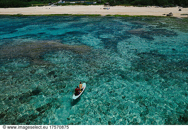 Brothers standup paddle boarding over coral reefs