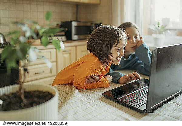 Brothers watching online lessons sitting on dining table at home